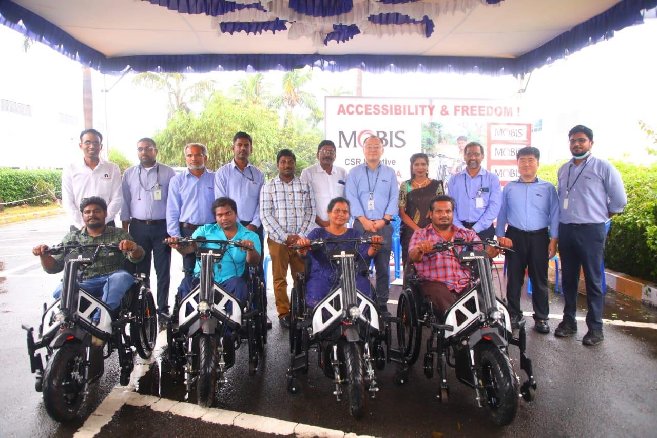 Beneficiaries seated on their new NeoMotion wheelchair bikes at a distribution ceremony, with SMART Foundation partners standing behind them